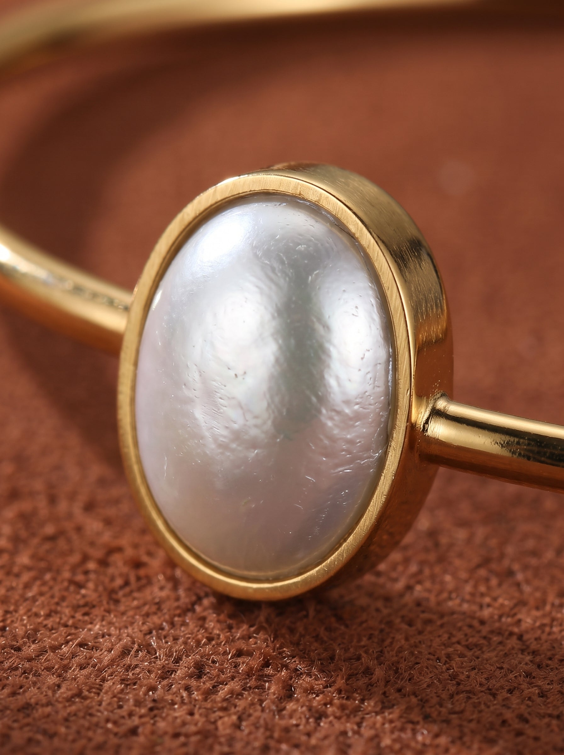 Close-up of a gold cuff bracelet featuring a lustrous 10mm oval freshwater pearl set in a polished gold bezel. The bracelet has a minimalist, open design. @pearl