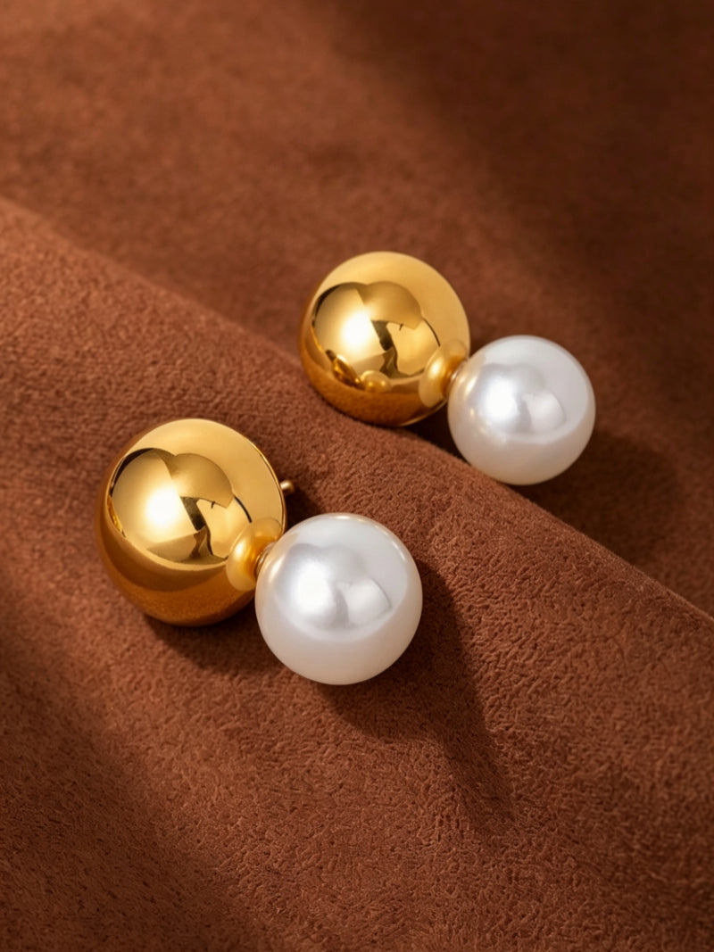 Sphere stud earrings featuring a polished gold-toned sphere paired with a luminous 10mm white Freshwater Pearl, displayed on a brown textured surface.