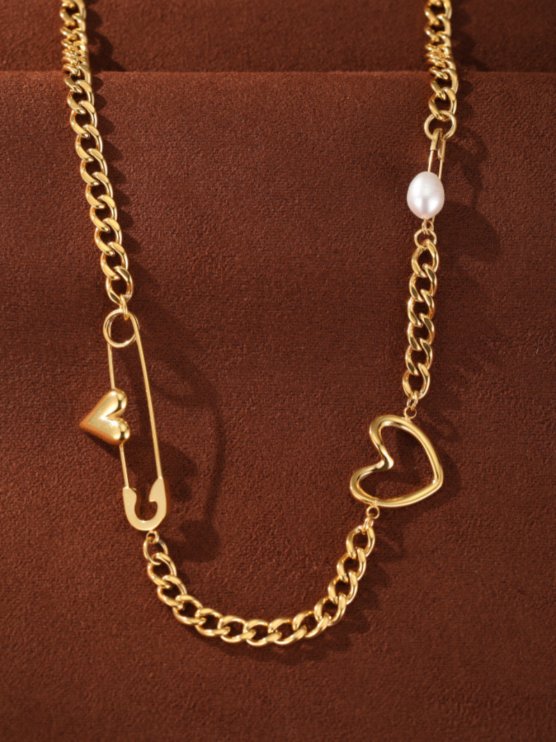 Collier ras-de-cou à chaîne gourmette imposante ton or avec une perle d'eau douce, une breloque cœur ouvert, et une épingle de sûreté avec une breloque cœur.