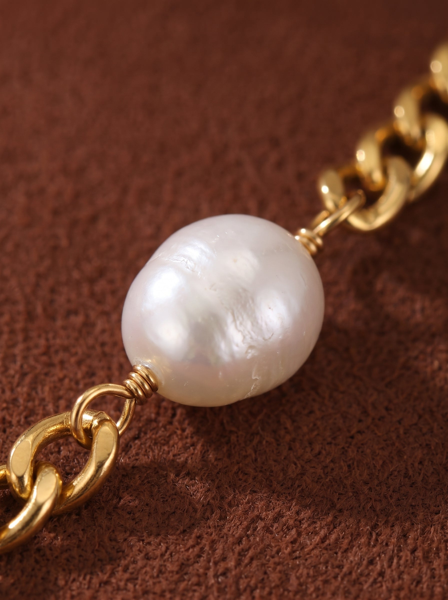 Gros plan d'un collier à chaîne gourmette imposante dorée présentant une seule et irrégulière perle blanche d'eau douce enveloppée de fil doré. @pearl