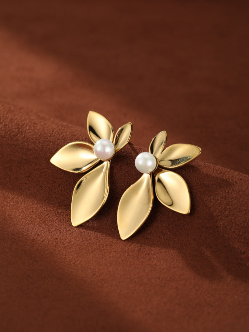 Boucles d'oreilles puces florales Sprout en perle d'eau douce présentant des pétales polis ton or formant un design floral avec une lustrée perle blanche d'eau douce en son centre, posées sur une surface texturée marron.