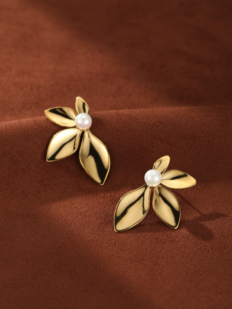 Boucles d'oreilles puces florales Sprout en perle d'eau douce en métal ton or avec de délicats détails pétales, chacune centrée d'une lustrée perle blanche, présentées sur fond texturé marron.