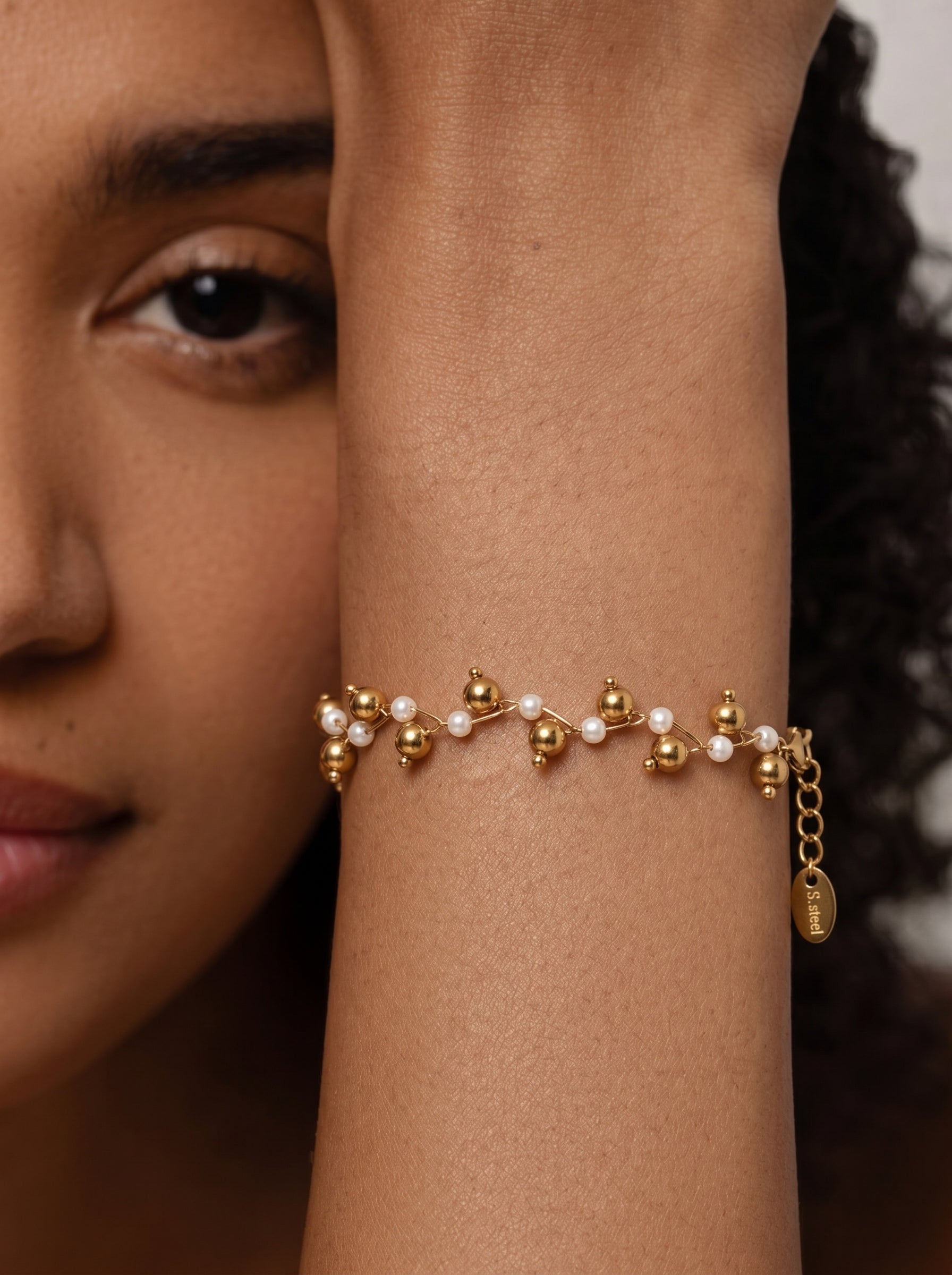 Stardust Mother of Pearl Beaded Bracelet with gold-toned spheres on a model's wrist. The bracelet features small white pearls and gold beads arranged in an organic, modern pattern. @model