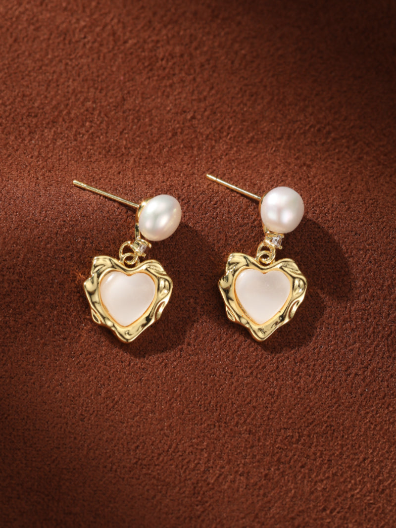 Delicate gold-tone stud earrings featuring a small white freshwater pearl dropping to a textured gold heart frame with a luminous white inlay. @pearl