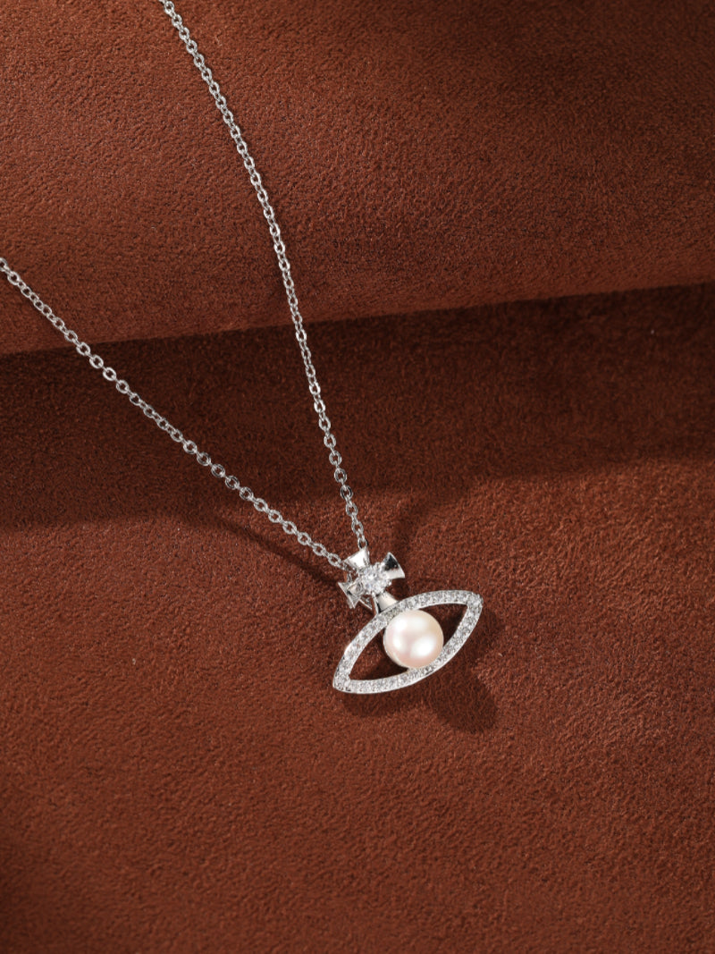 Stellar Gaze necklace featuring an eye-shaped pendant encrusted with small diamonds, a central 6mm button freshwater pearl, and a small cross detail above, all on a delicate silver chain. @pearl