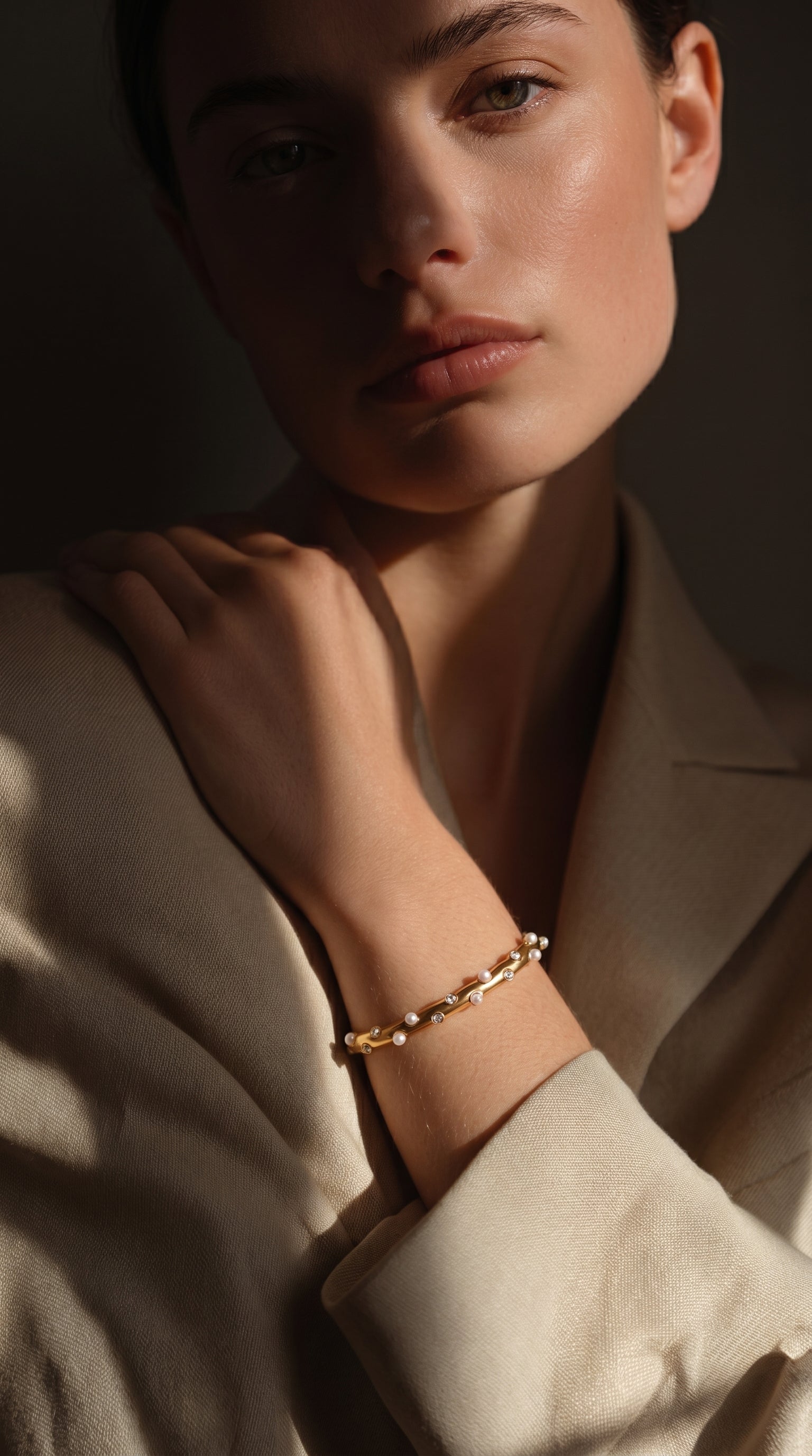 Close-up of a model wearing the Stellar Path Imitation Pearl Cuff Bracelet on her wrist, showcasing its modern design with small white pearls and sparkling accents on a gold-tone cuff. The image is softly lit, highlighting the bracelet's texture and shine. @model