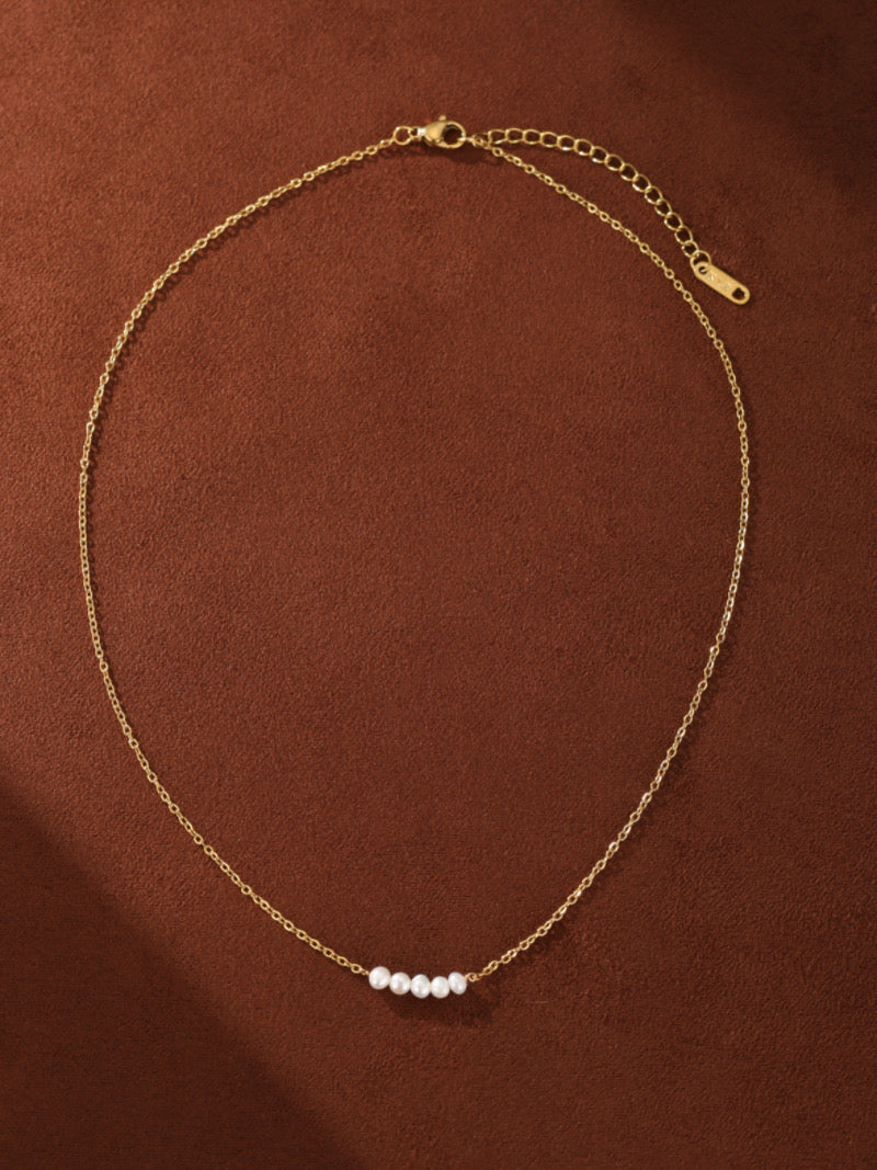 A delicate gold-toned chain necklace featuring a small cluster of seven tiny white freshwater pearls arranged in a gentle curve.
