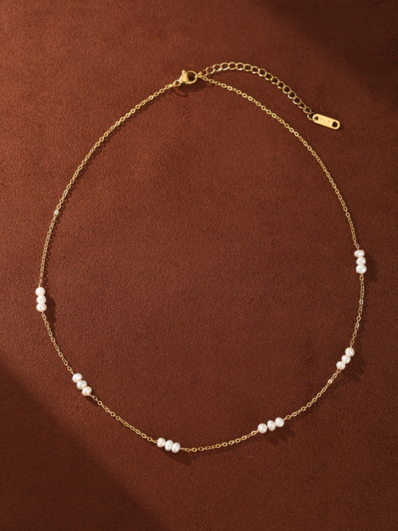 Stellaris layered necklace with delicate gold chains and scattered 2mm white freshwater button pearls on a brown background.