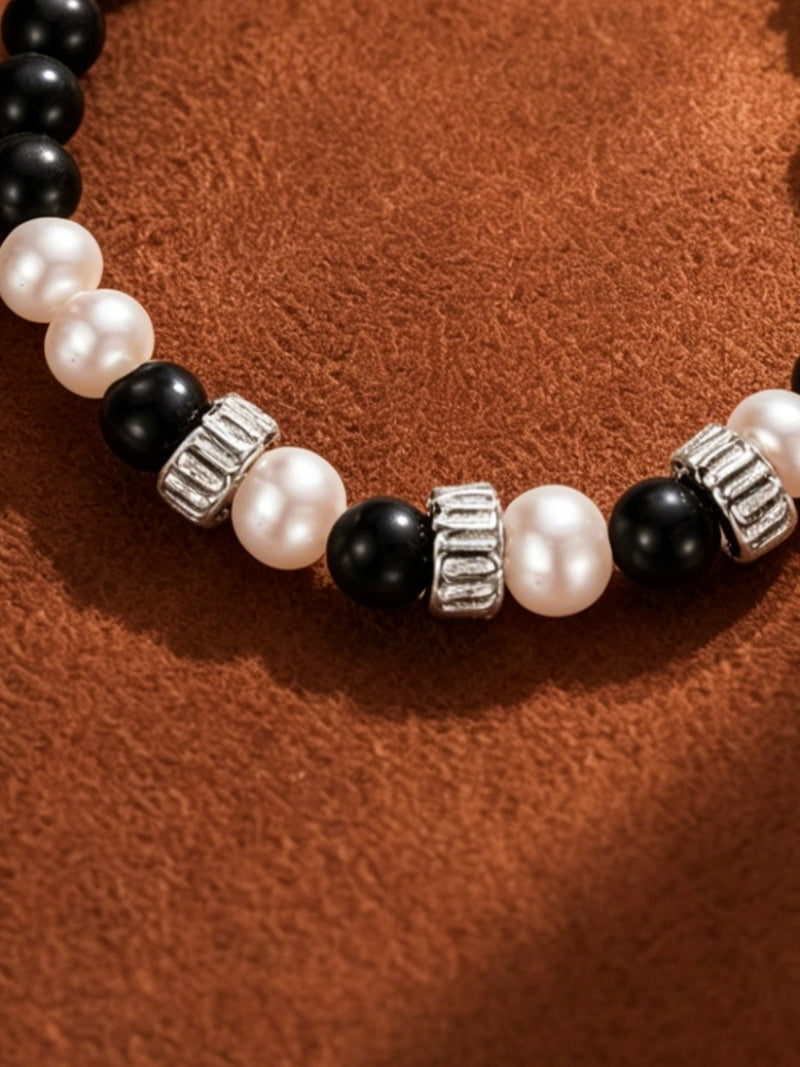 Close-up of Strata bracelet featuring alternating 8mm white button freshwater pearls and black spherical beads, separated by silver-toned cylindrical spacers, set against a textured brown background.