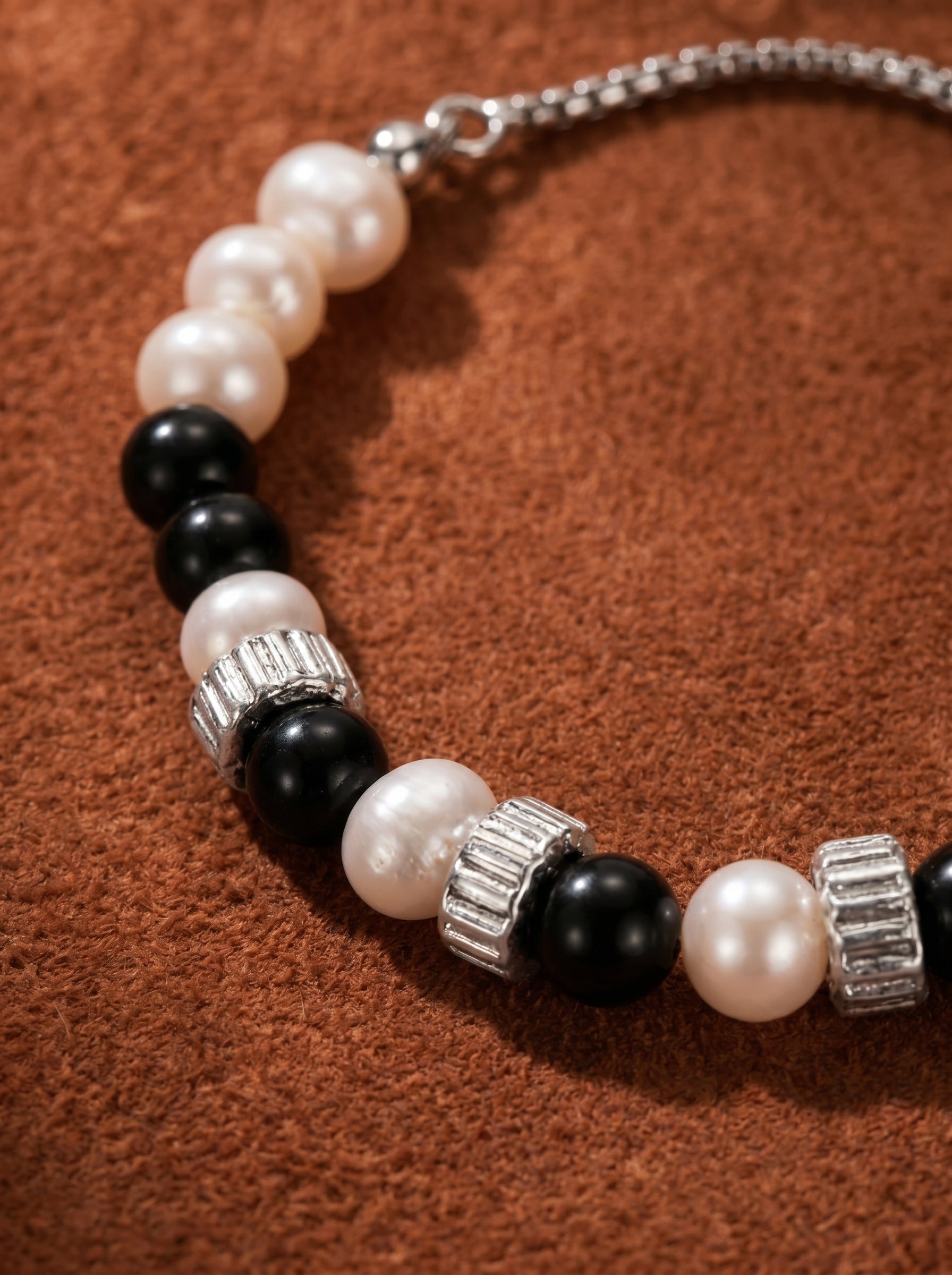 Strata bracelet with alternating 8mm white button freshwater pearls and black spherical beads, separated by silver-toned cylindrical spacers, on a textured brown background. @pearl