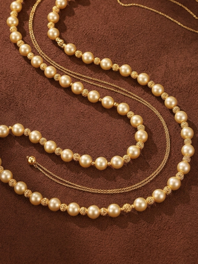 Three strands of long golden freshwater pearl necklaces with delicate gold chains and textured gold beads between the pearls, laid out on a brown textured background.