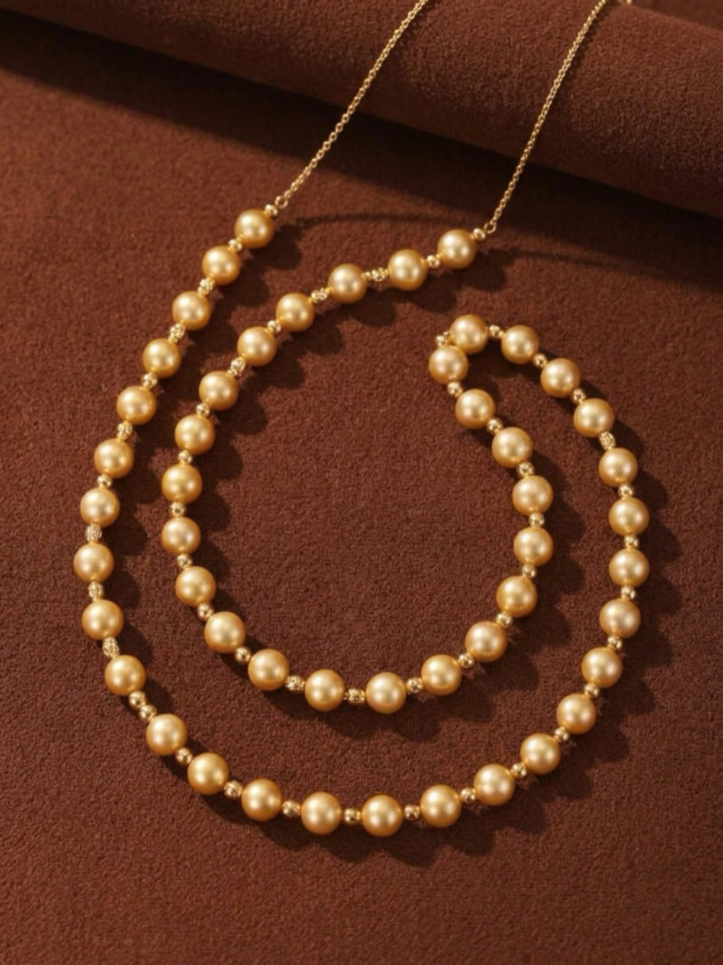 Sunlit Strand long beaded necklace featuring 9mm golden freshwater pearls strung on a delicate gold chain, displayed against a brown textured background.