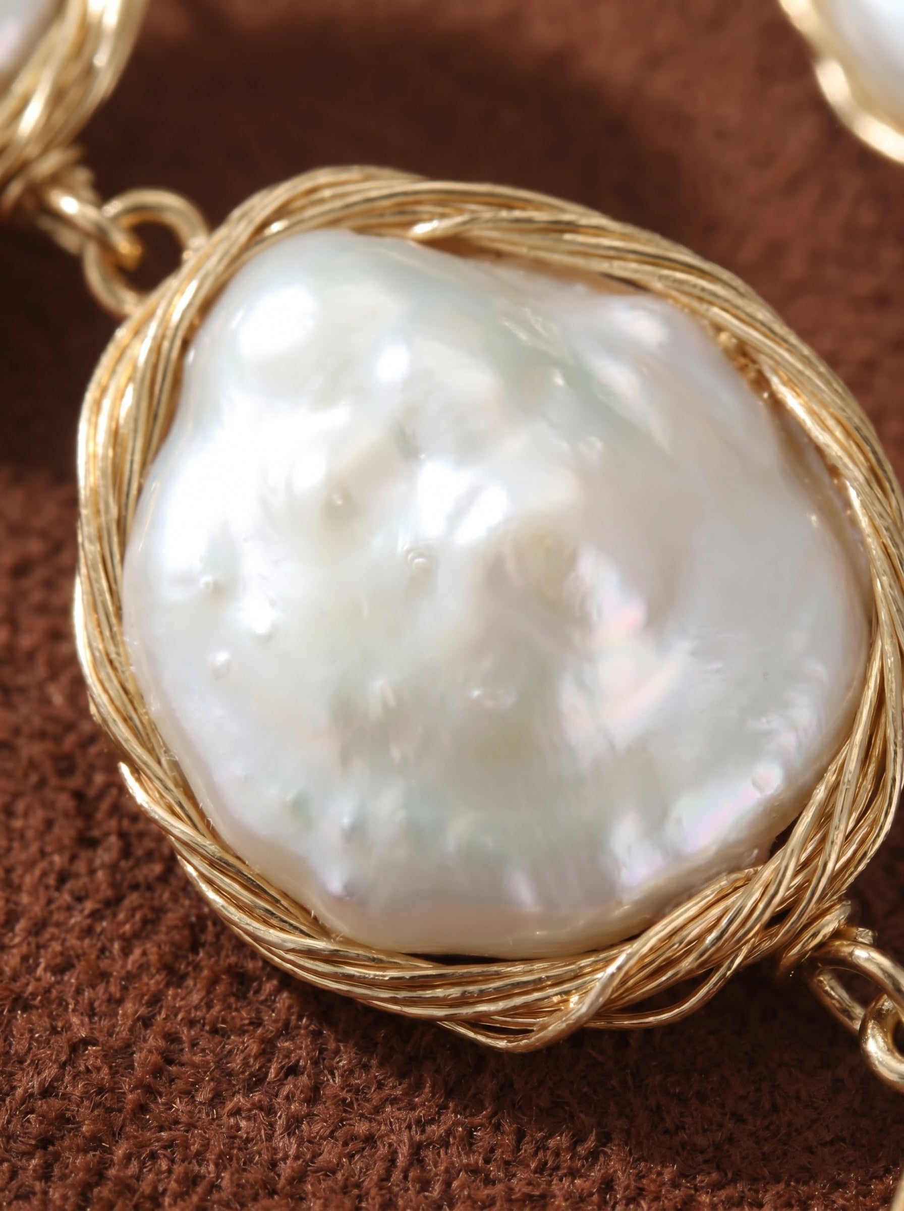 Close-up of a large, irregular white freshwater pearl with a luminous sheen, wrapped in delicate gold-toned wire, as part of the Sway Triple Dangle Earrings. @pearl