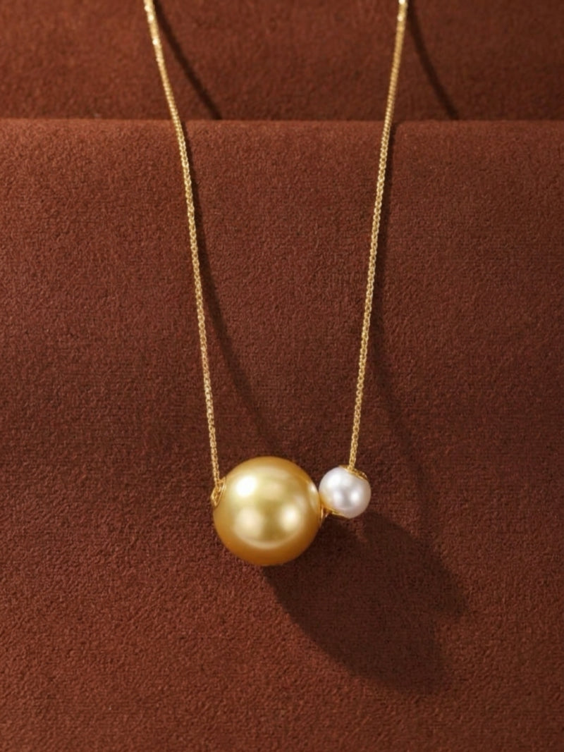 A delicate gold chain necklace featuring a large, lustrous golden South Sea pearl and a smaller, radiant white Akoya pearl suspended side-by-side.