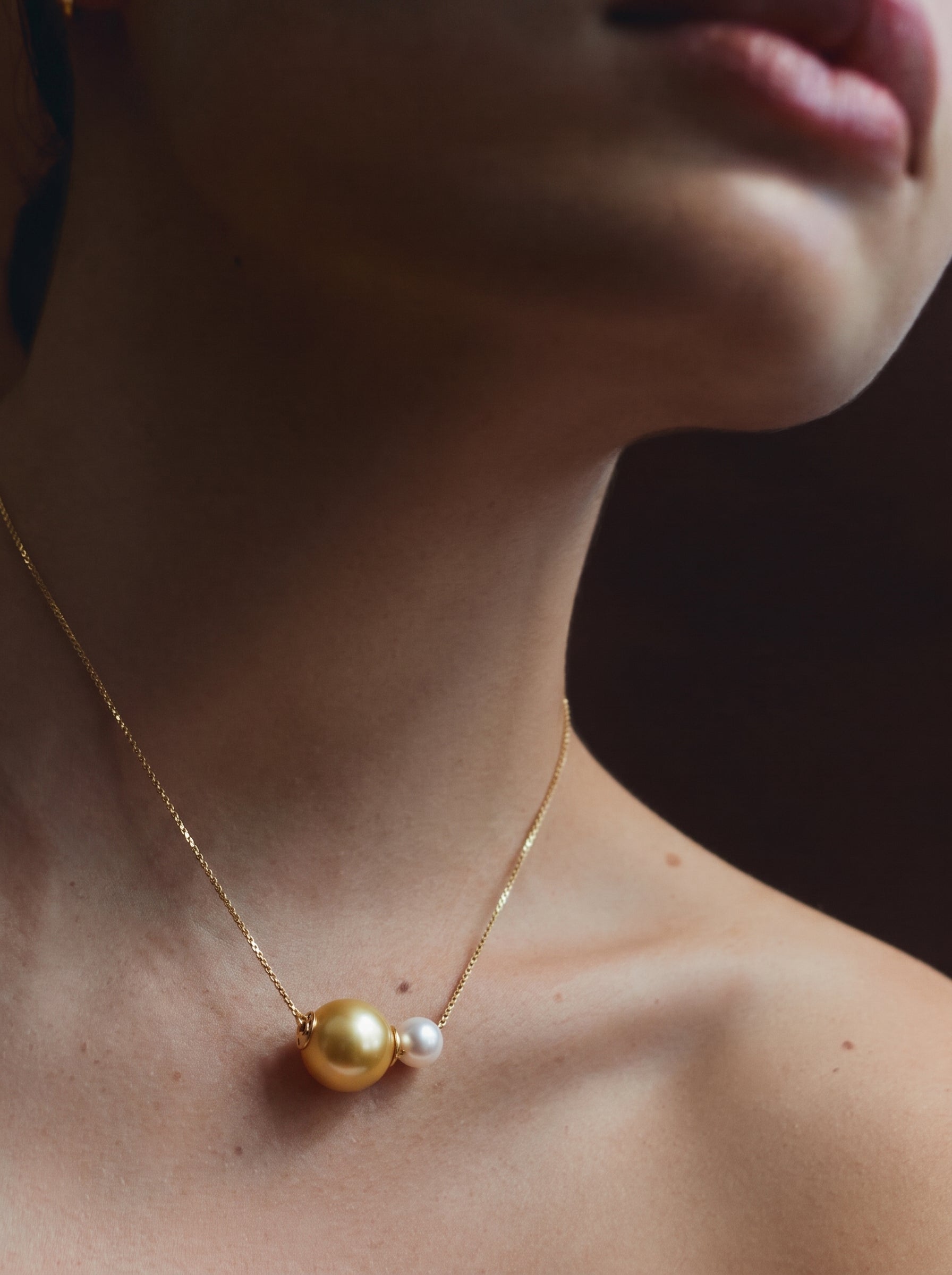 A model wearing a delicate gold chain necklace featuring a large golden South Sea pearl and a smaller white Akoya pearl pendant. @model