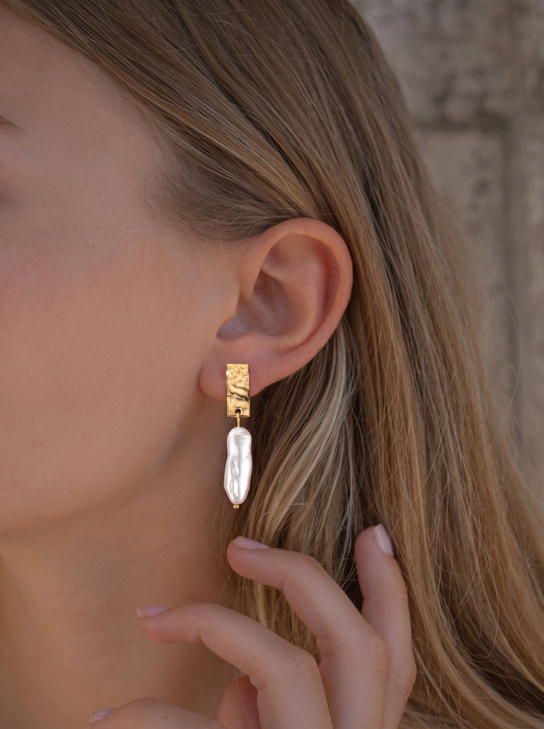 Boucles d'oreilles goutte en perle d'eau douce Terra présentant une puce rectangulaire martelée ton or et une grande et irrégulière goutte de perle baroque blanche. @model
