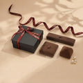 A dark grey gift box tied with a burgundy ribbon featuring the brand name. Beside it are three brown velvet jewelry boxes and a few pearls. @shared