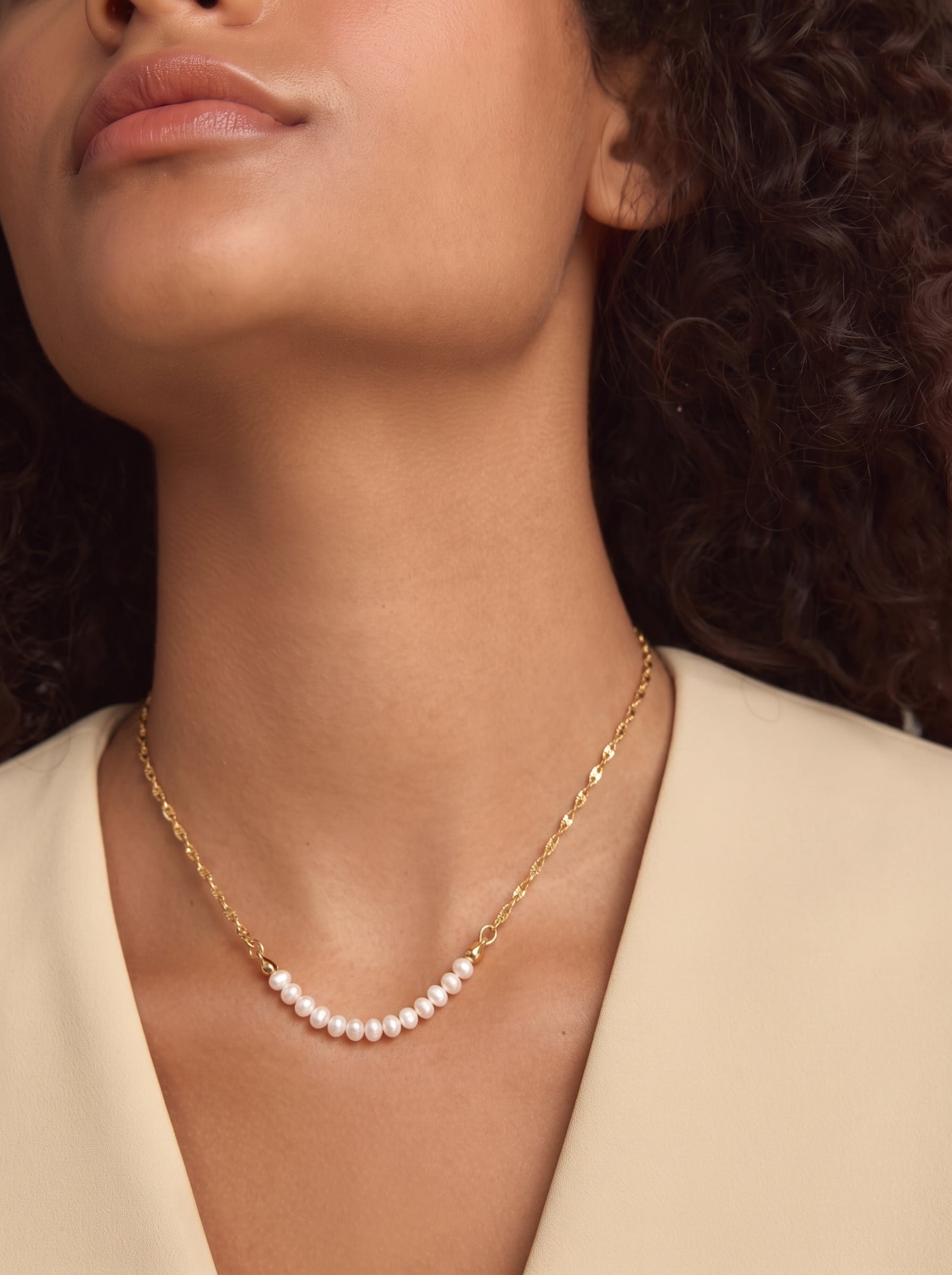 Photo en gros plan d'une mannequin portant le collier à chaîne perlée Trace en perle d'eau douce, présentant une délicate chaîne ton or ornée d'un subtil arc de petites et lustrées perles blanches d'eau douce. @model