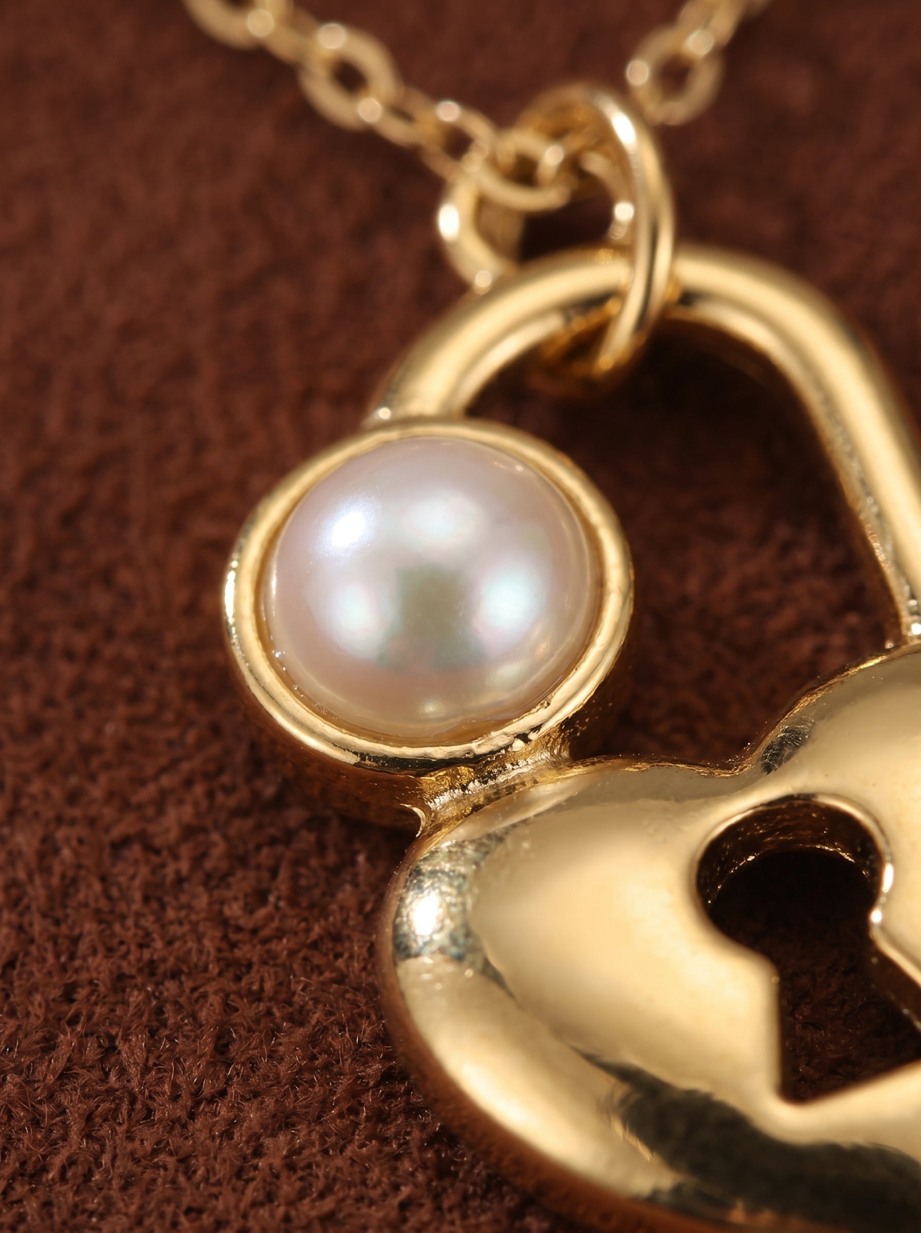 Gros plan d'un pendentif de collier ton or présentant un cadenas en forme de cœur avec une lustrée perle bouton blanche d'eau douce et un détail trou de serrure. @pearl