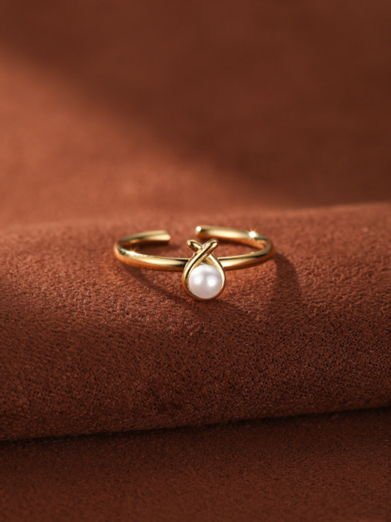 Gold-toned cuff ring with an intertwined knot design cradling a luminous white freshwater pearl.