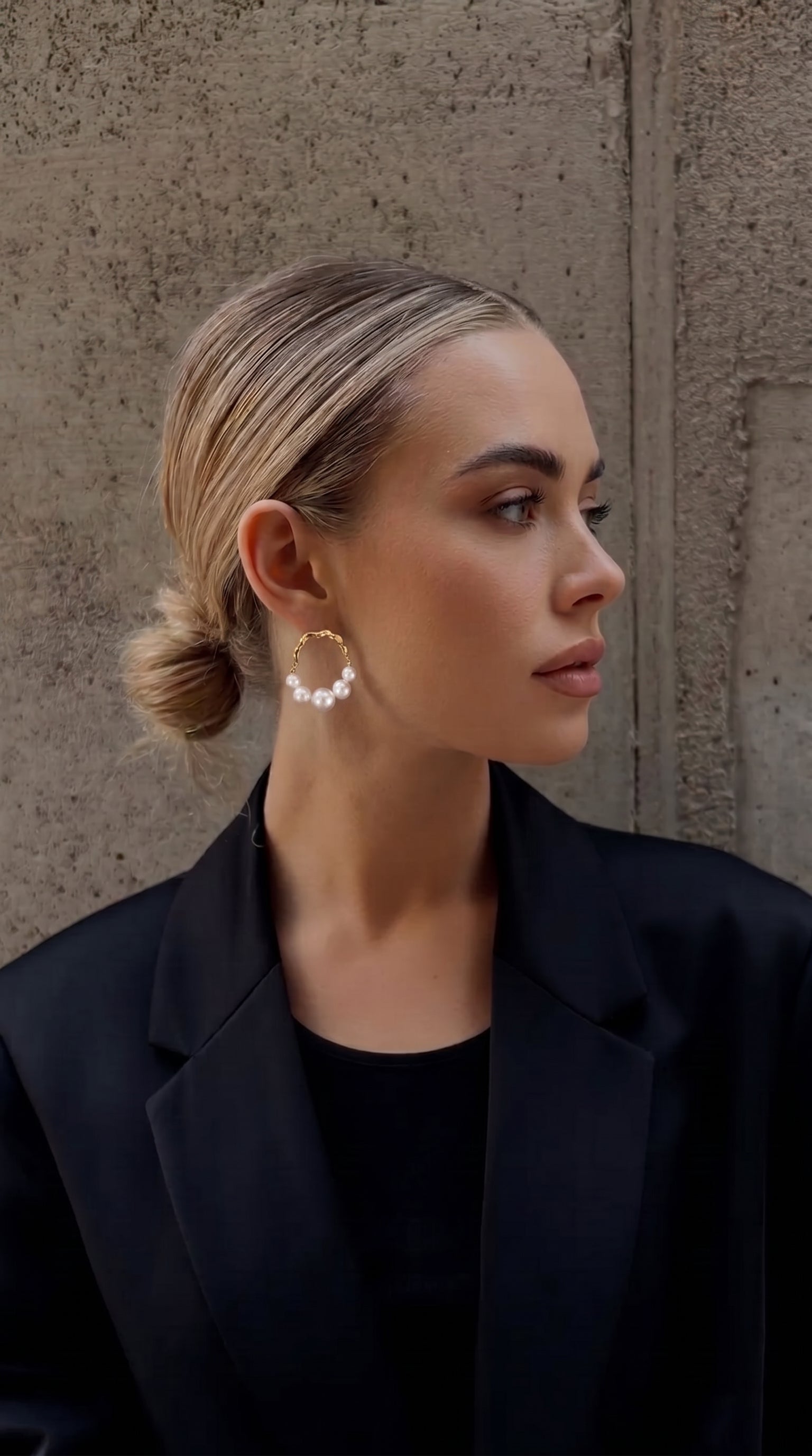 Mannequin portant les créoles ondulées Undine en perle d'eau douce avec une forme organique ton or et des perles blanches graduées, associées à un blazer noir. @model