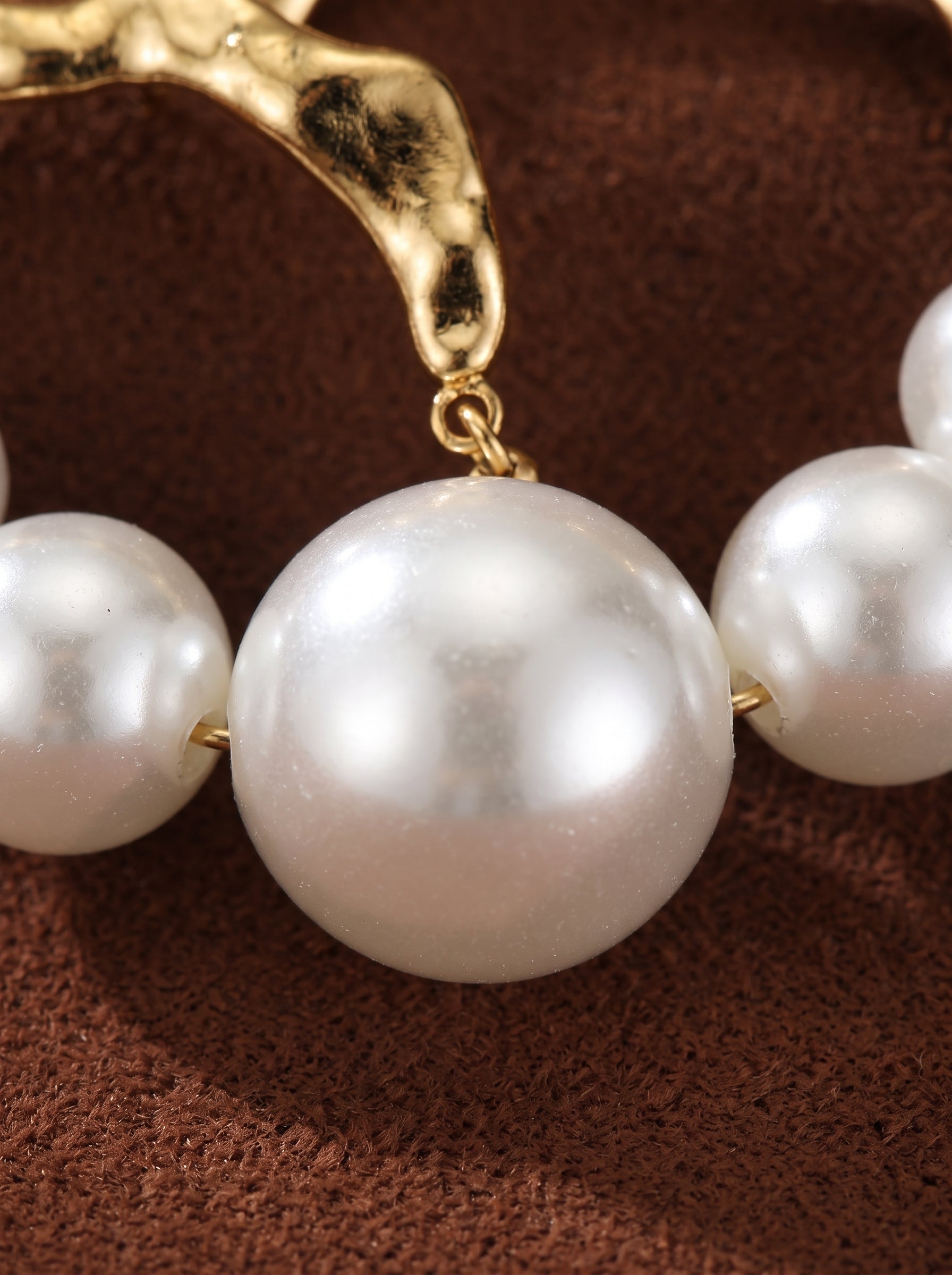 Gros plan des créoles ondulées Undine en perle d'eau douce présentant un dessus ondulé doré et des perles rondes blanches graduées d'eau douce de tailles variées. @pearl
