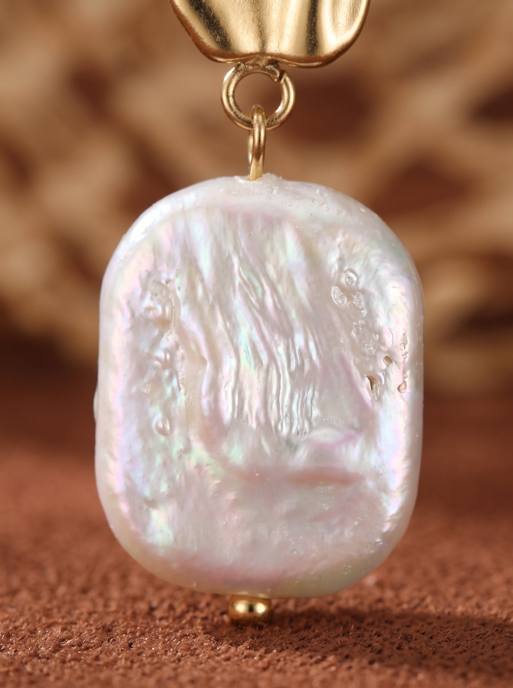 Gros plan d'une seule boucle d'oreille goutte Undulate en perle d'eau douce, mettant en valeur la puce dorée à la texture organique et la lustrée perle baroque blanche de forme irrégulière aux reflets irisés. @pearl