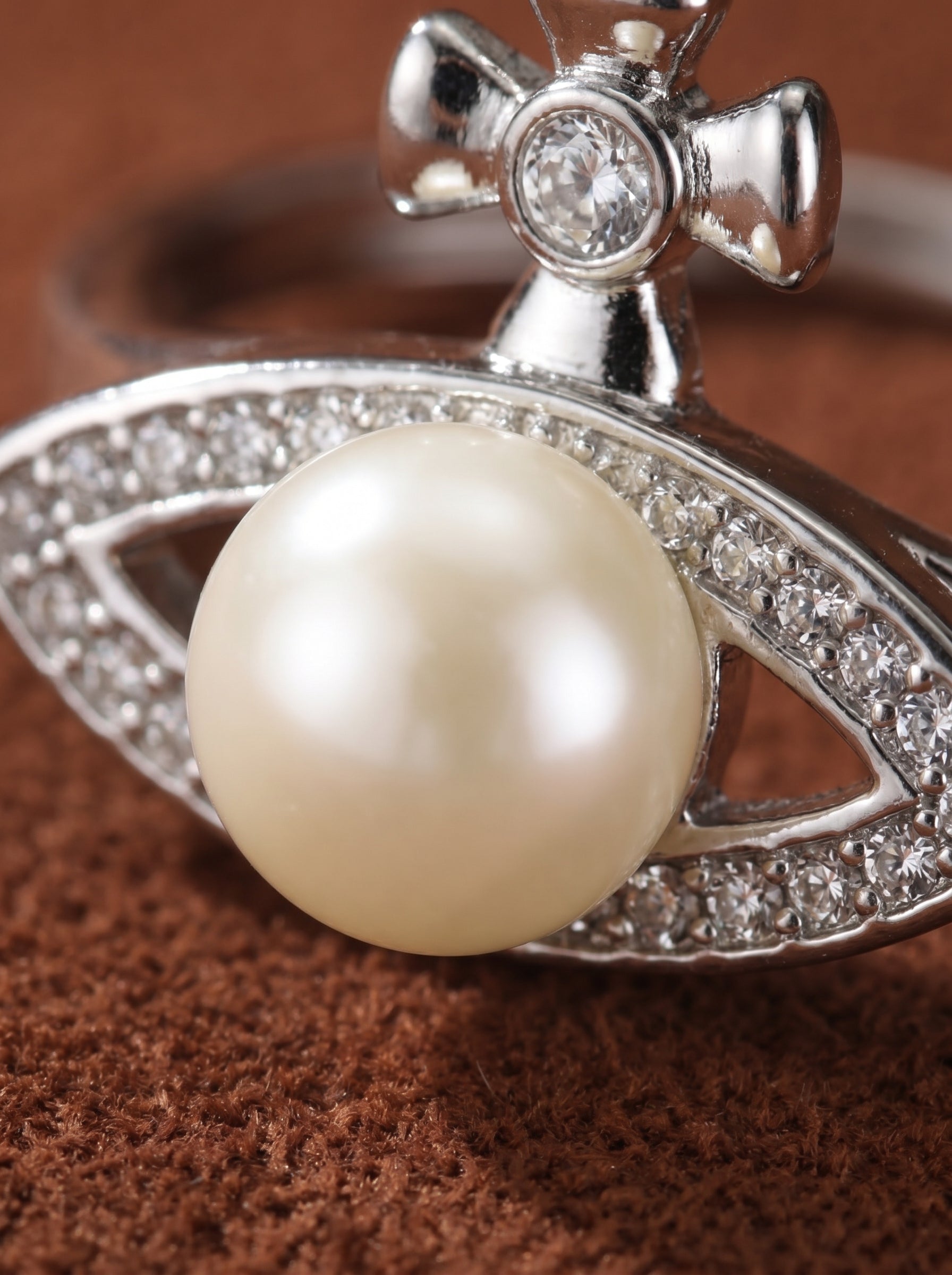Silver-toned cuff ring featuring a luminous freshwater pearl, a cross motif, and sparkling pave details on a brown textured surface. @pearl