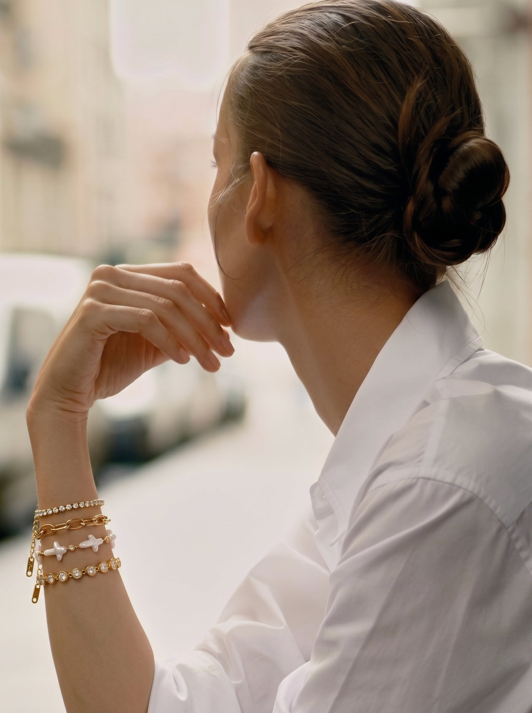 A woman wearing the Verge Freshwater Pearl Cross Chain Bracelet, featuring unique cross-shaped white pearls and gold chains, in a thoughtful pose outdoors. @lifestyle