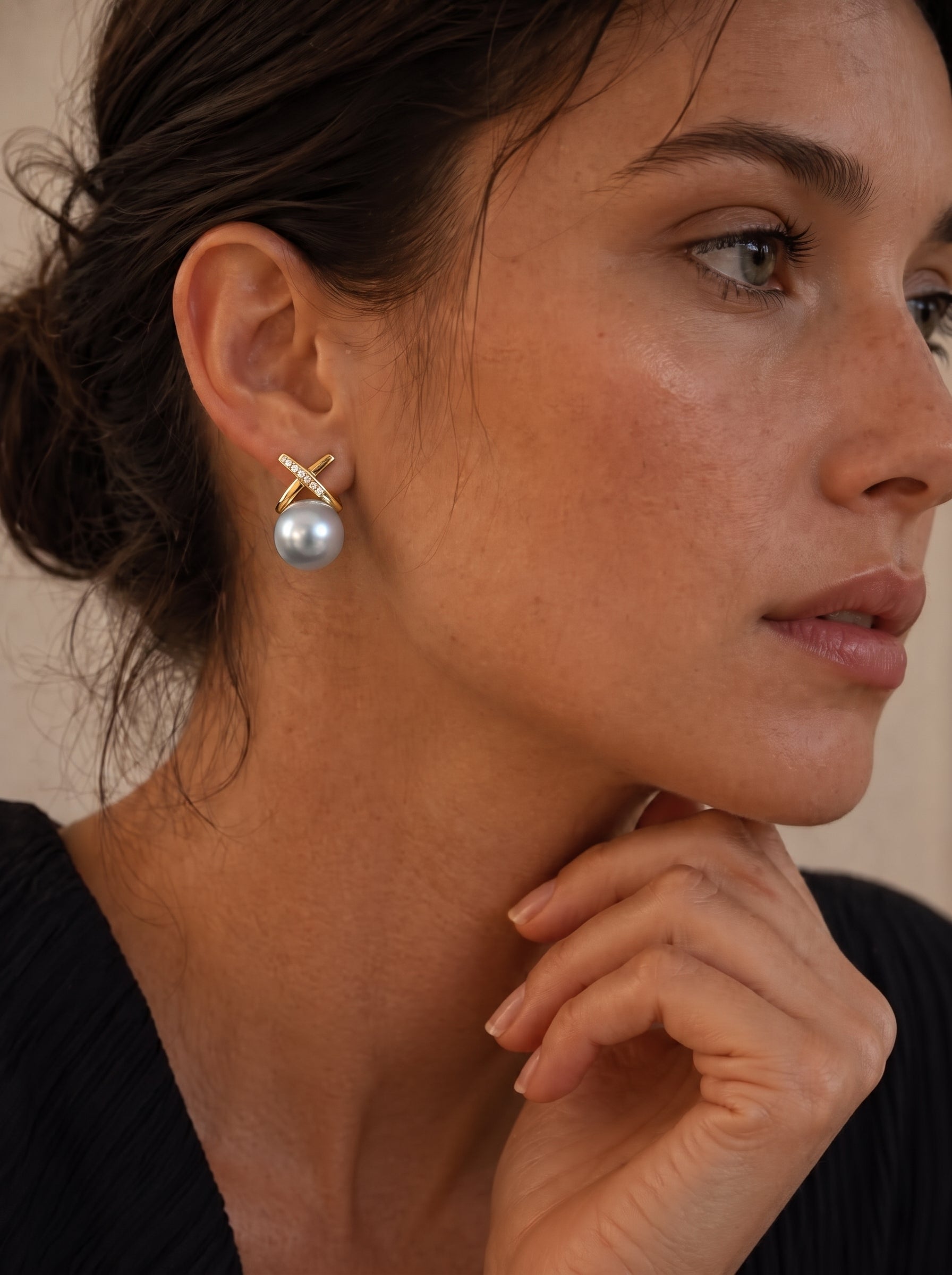 Close-up of a woman wearing Veritas Akoya Pearl Cross Stud Earrings, featuring gold-toned cross motifs with pavé crystals and a lustrous grey Akoya pearl. @model