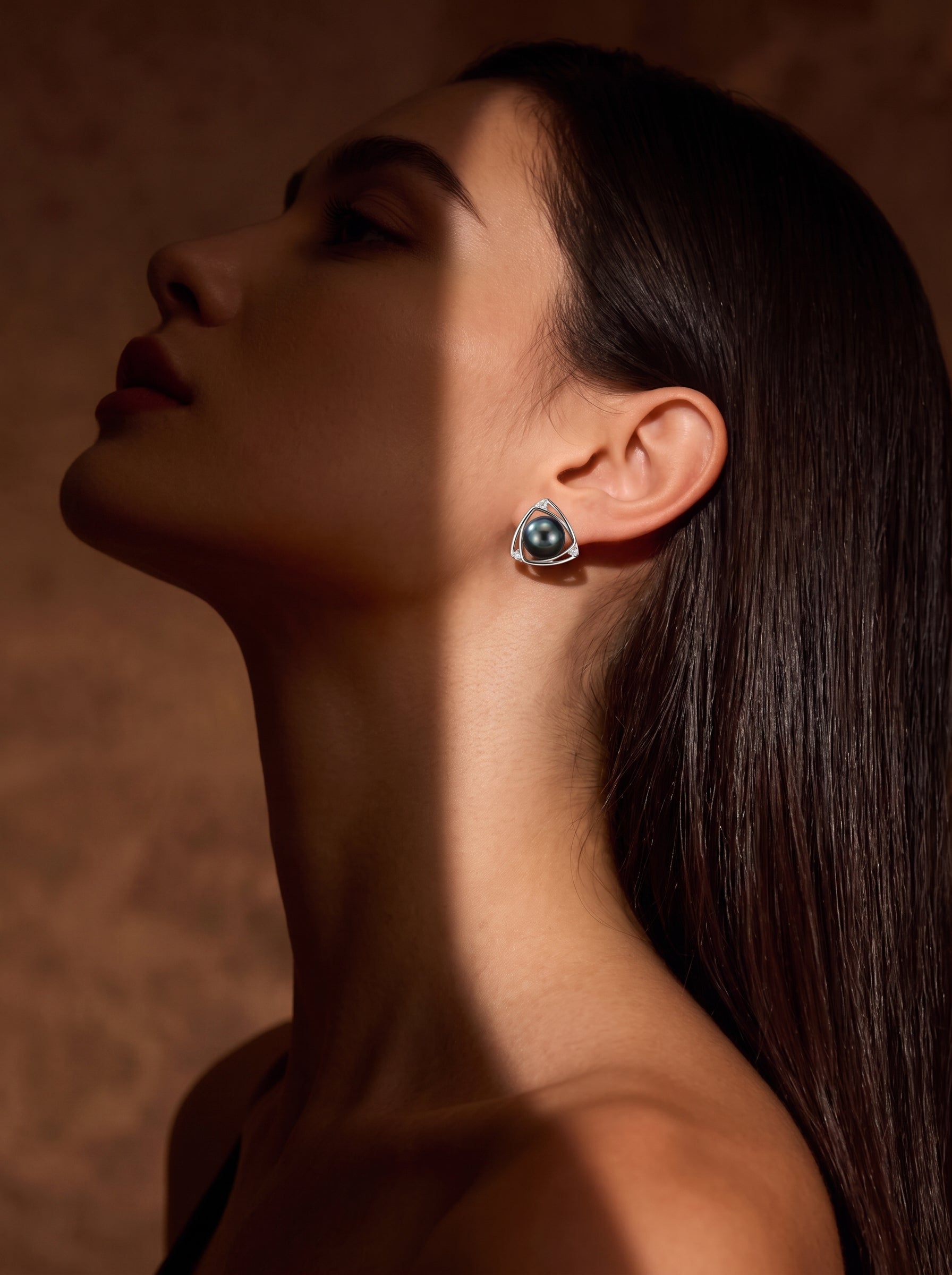 Close-up of a woman wearing Vertex Tahitian Pearl Triangle Stud Earrings, featuring a black pearl set in a silver triangle frame with pavé accents. @model