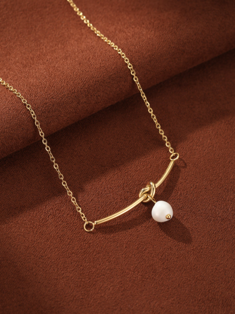 Verve gold chain necklace featuring a curved bar with a knot detail and a single white freshwater pearl drop. @pearl