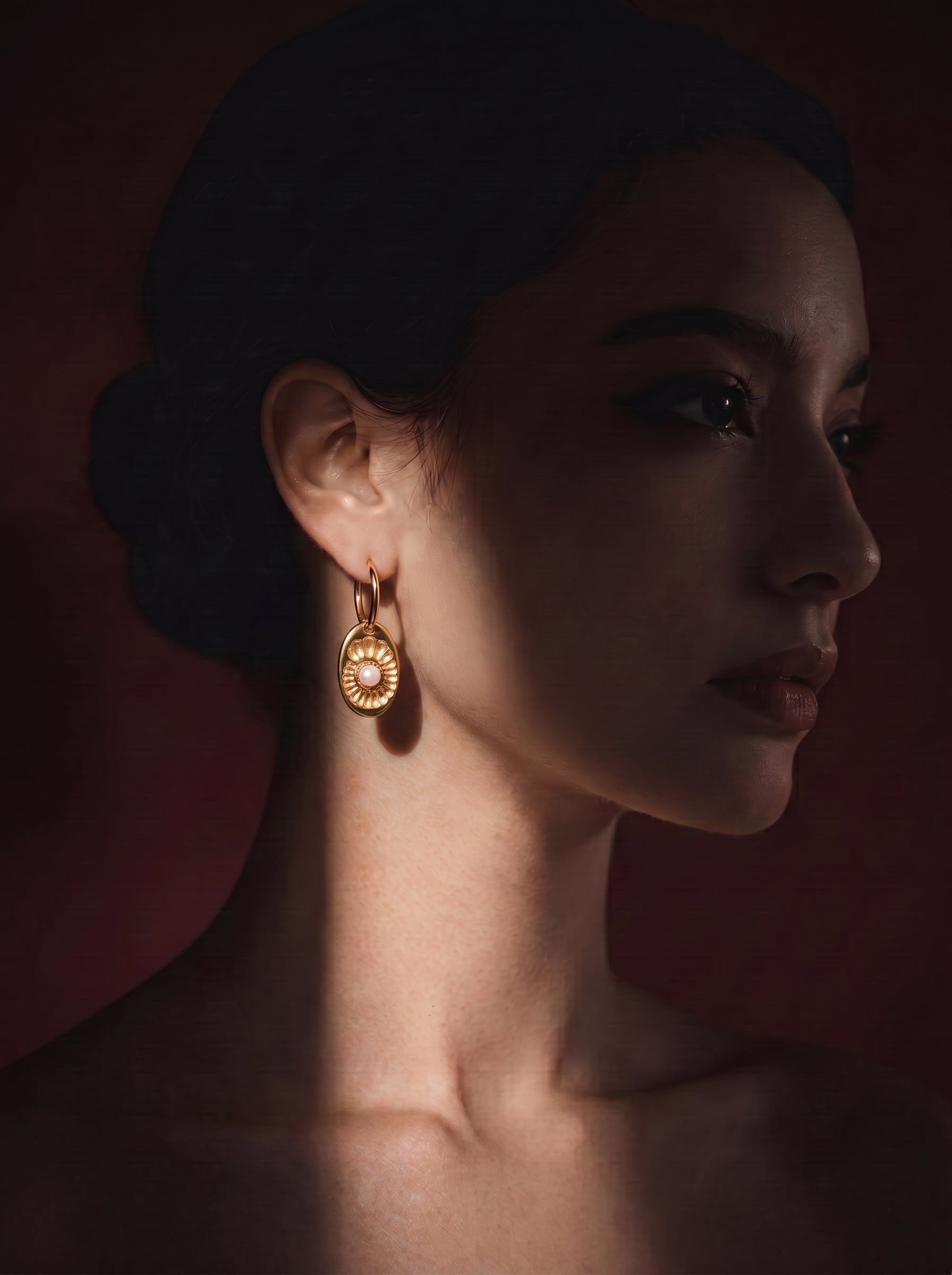 Close up of a model wearing Vesica freshwater pearl spiral hoop drop earrings, featuring a golden oval charm with a spiral pattern and a luminous white pearl. @model