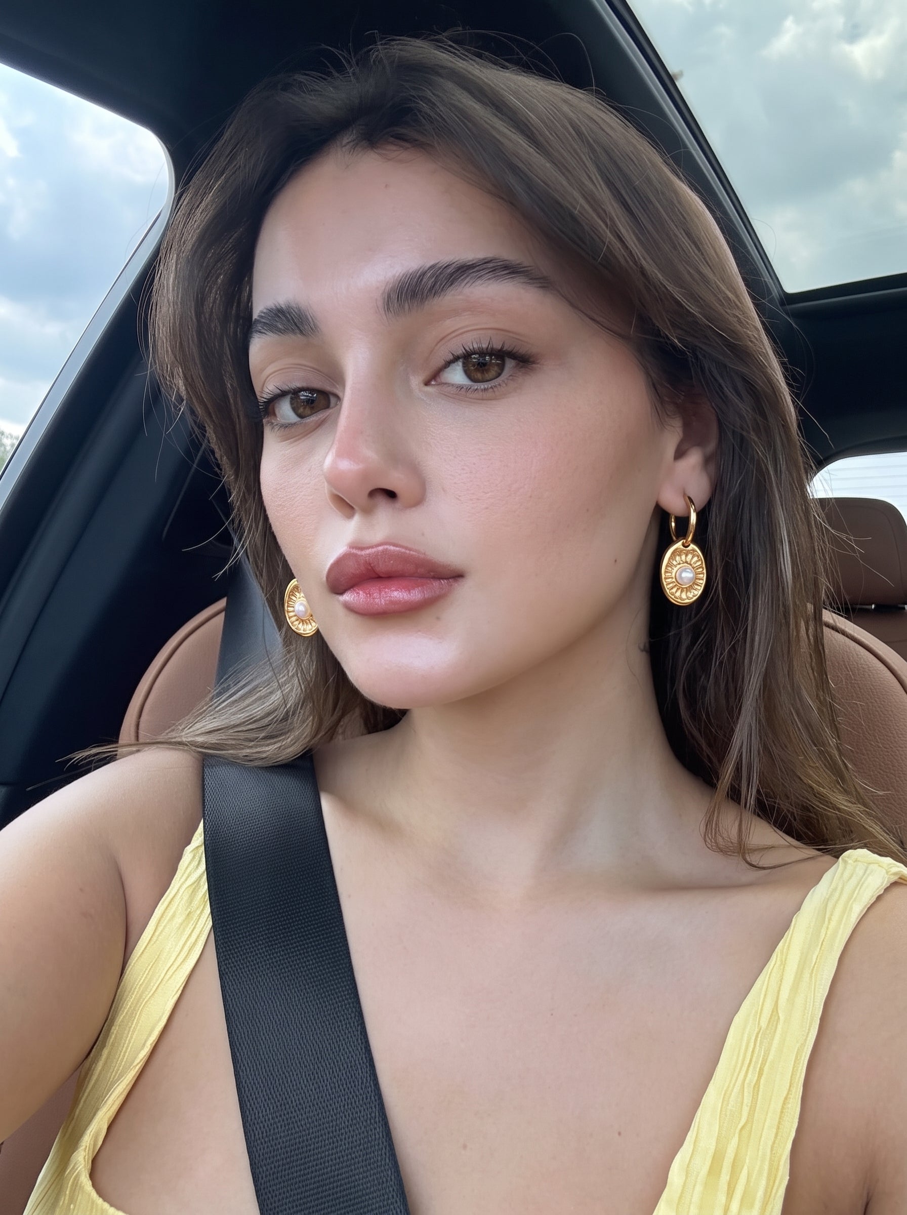 Model wearing Vesica Freshwater Pearl Spiral Hoop Drop Earrings in a car, showcasing the gold oval charms with a pearl accent and spiral pattern. @lifestyle
