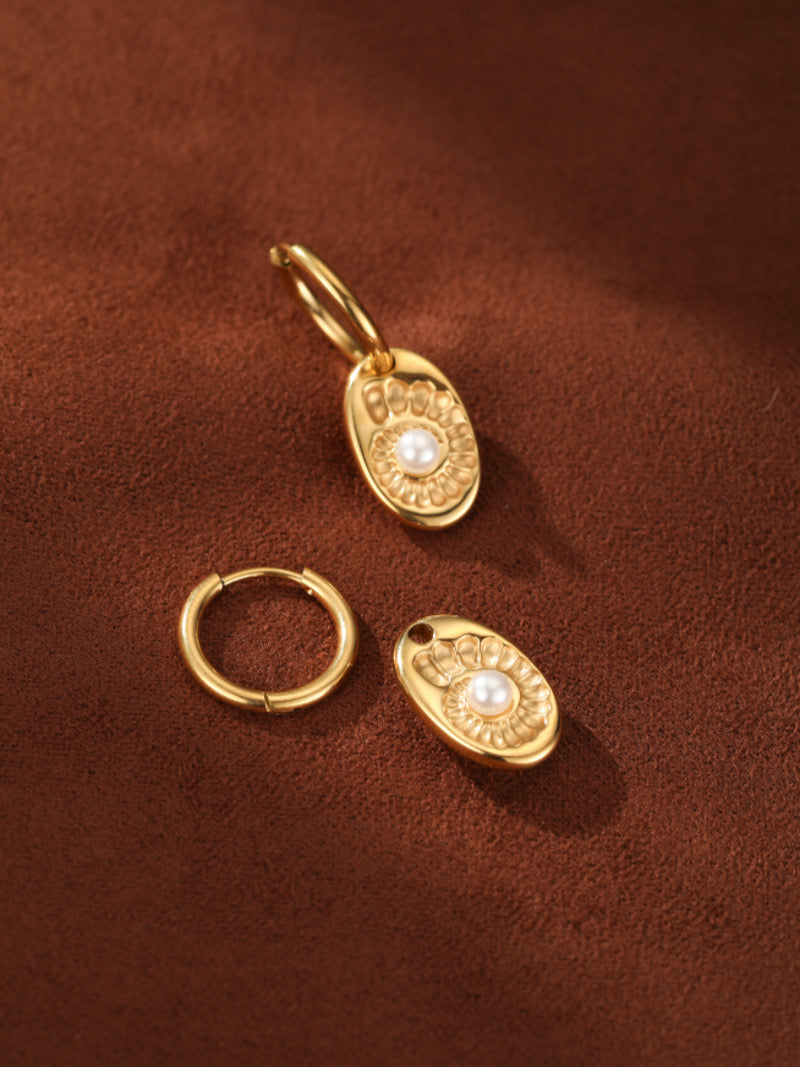 Gold spiral hoop drop earrings with a white freshwater button pearl set in an oval charm, displayed on a brown textured surface.