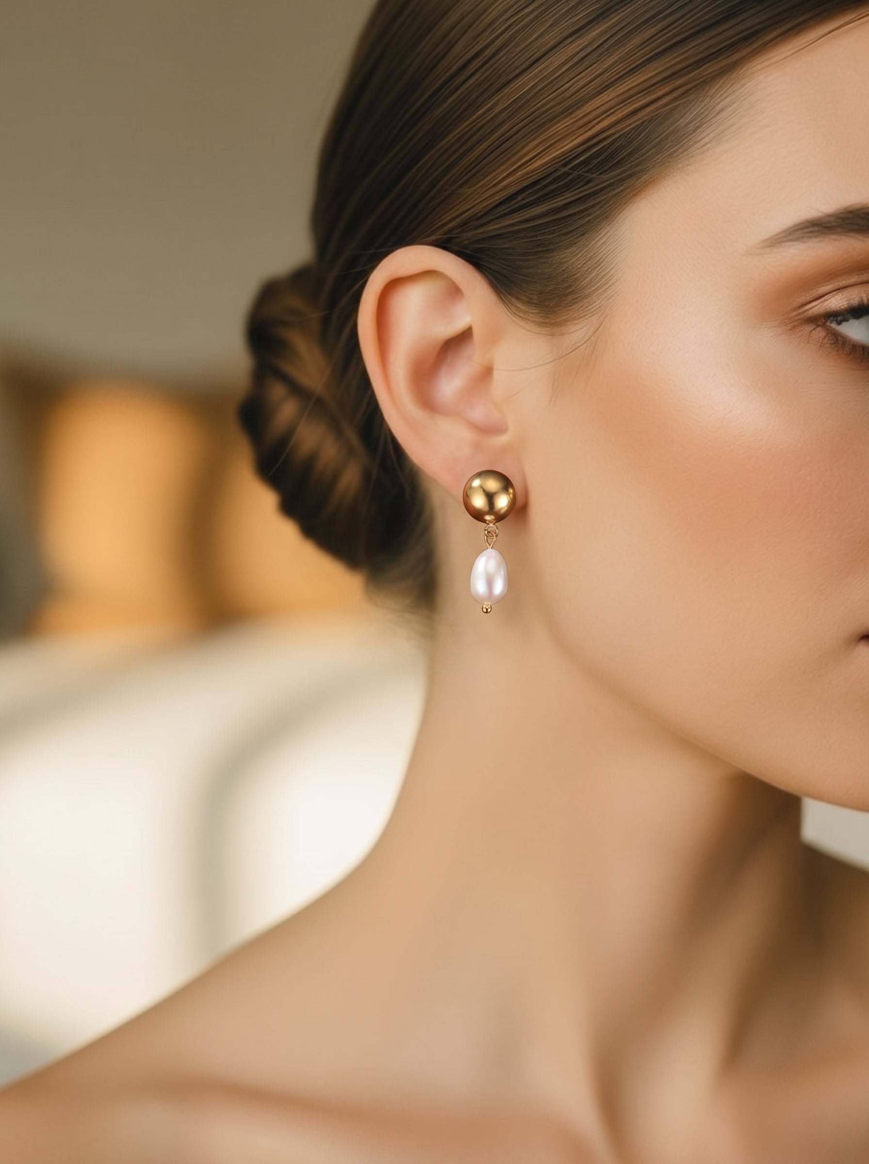 Gros plan de l'oreille d'une femme portant les boucles d'oreilles goutte Vesper en perle d'eau douce, présentant une puce sphère dorée et une seule perle en larme pendant en dessous. @model