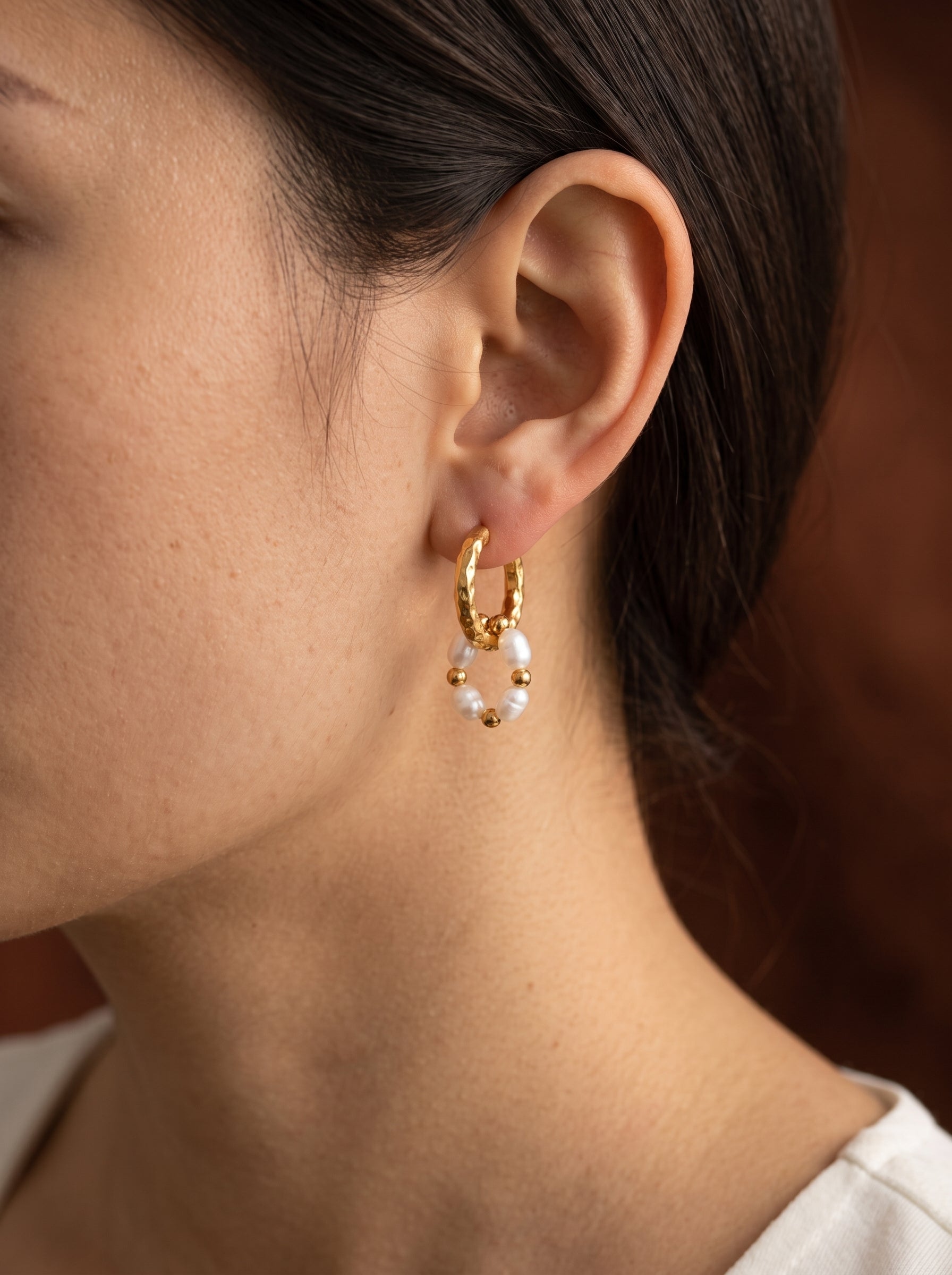 Gros plan de l'oreille d'une femme portant des boucles d'oreilles goutte ton or ornées de petites perles blanches d'eau douce et de perles dorées. @model