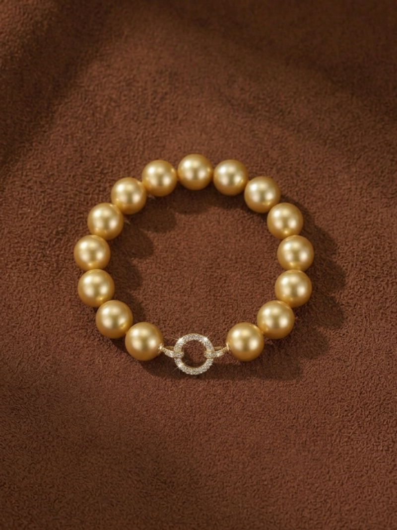 A close-up shot of a Vibrant Loop bracelet featuring large, lustrous golden freshwater pearls strung together and fastened with a circular clasp encrusted with small, sparkling diamonds.