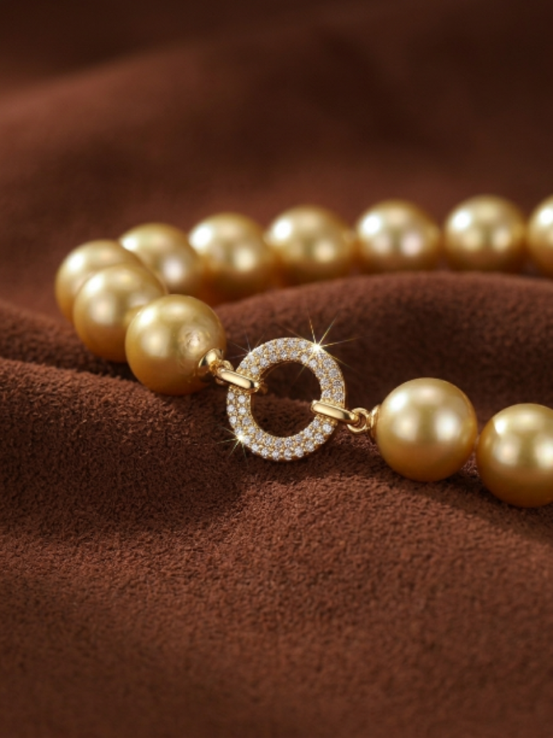 Close-up of a Vibrant Loop bracelet featuring a strand of lustrous 10 mm round golden freshwater pearls and a sparkling circular clasp encrusted with pavé-set diamonds, resting on a textured brown fabric.