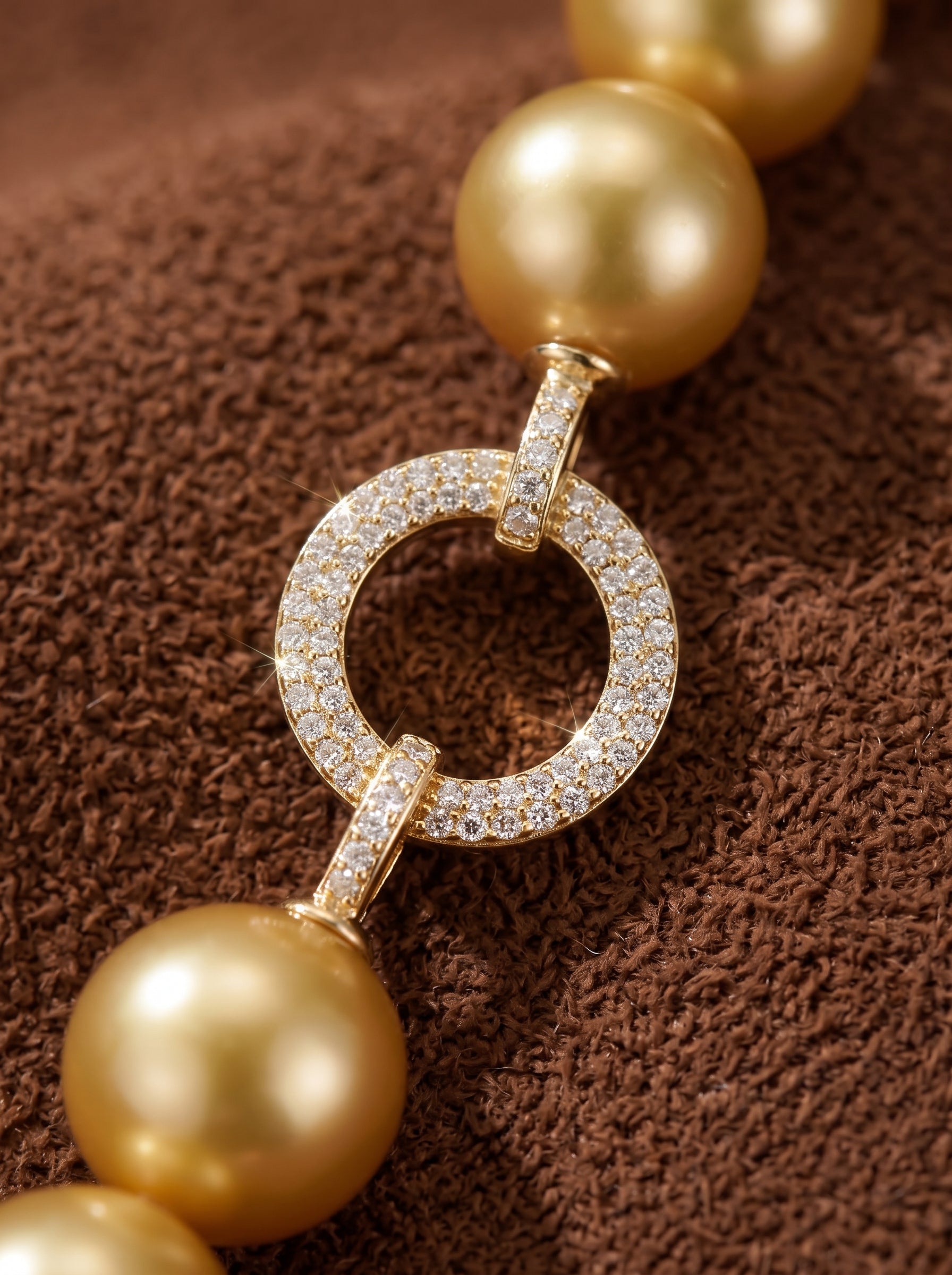 A close-up shot of a Vibrant Loop bracelet featuring large, lustrous golden freshwater pearls linked by a circular clasp encrusted with small diamonds. The bracelet is displayed on a textured brown background. @pearl