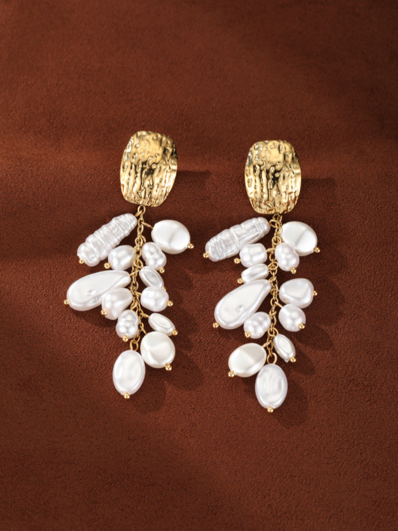 Une paire de boucles d'oreilles pendantes Vine en perle baroque d'eau douce présentant des puces martelées ton or et des cascades de perles blanches irrégulières enfilées sur de délicates chaînes.