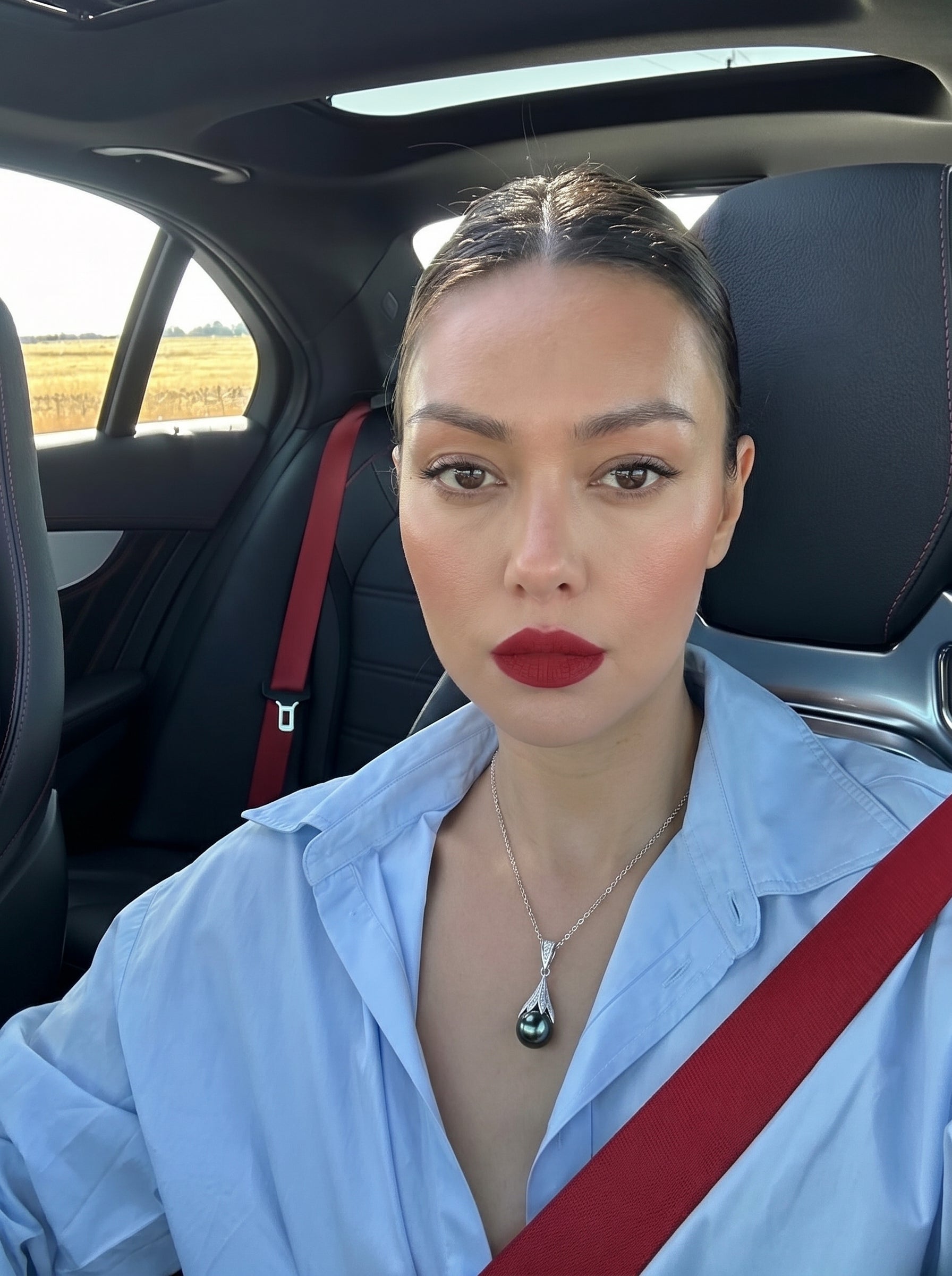 Woman wearing the Vortex Tahitian Pearl Drop Necklace with a black pearl and diamond-encrusted cap, seated in a car with a red seatbelt visible. @lifestyle #lifestyle