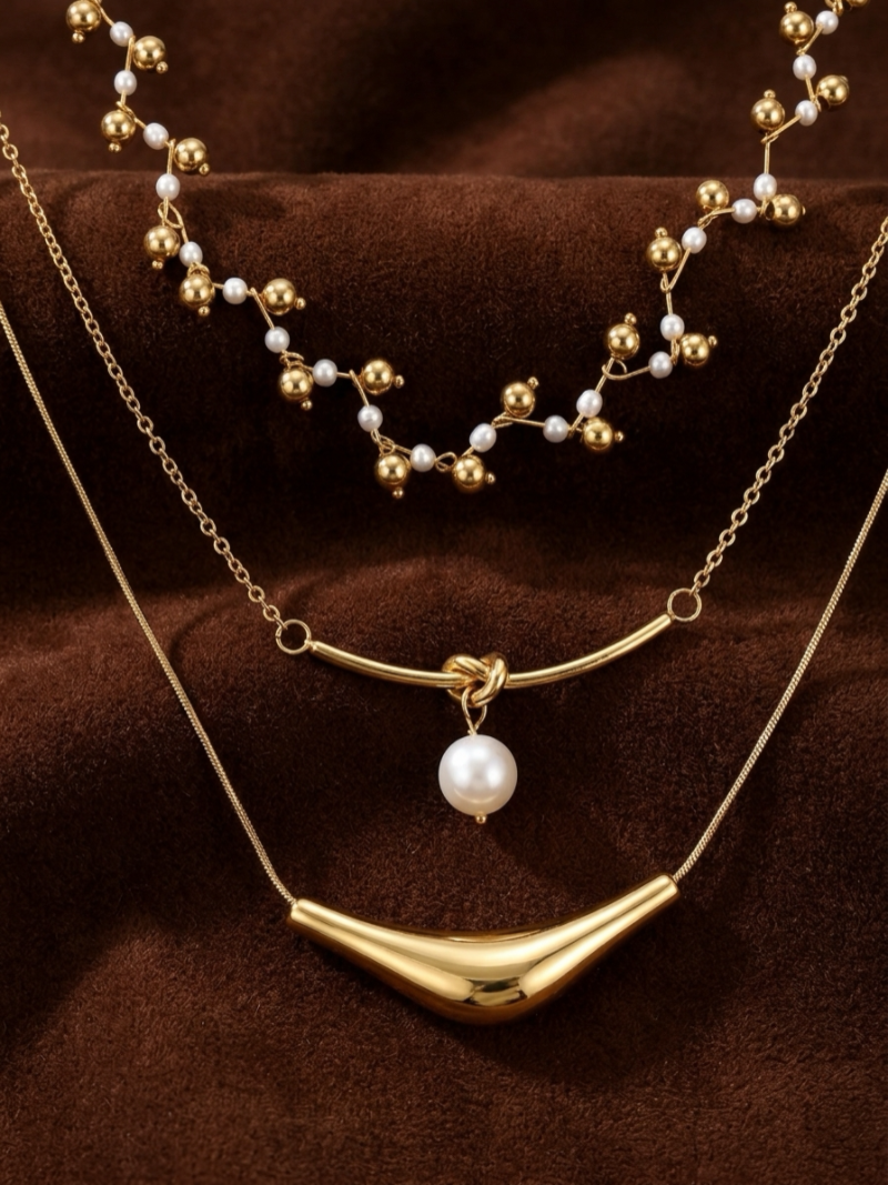 Voyage layered necklace with delicate freshwater pearls and gold beads on the top strand, a central strand with a knot and a white pearl, and a sculptural gold-tone bar on the bottom strand.