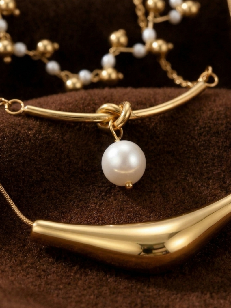 Voyage layered necklace featuring a knot detail with a single white freshwater pearl, a strand of small pearls and gold beads, and a sculptural gold-tone bar. @pearl