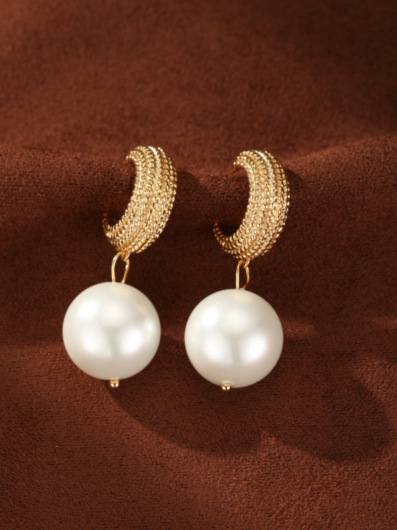 Gold-toned woven orb hoop earrings with a large white imitation pearl drop. These contemporary earrings are elegant and sophisticated.